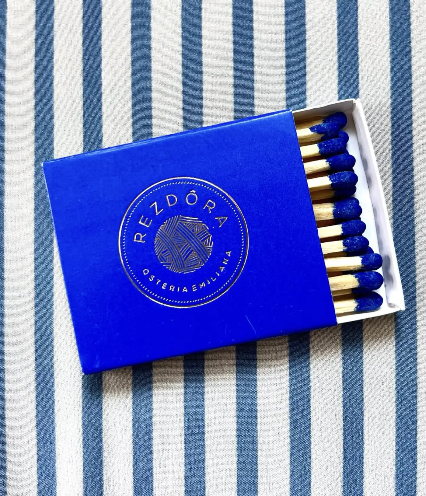 A cobalt blue matchbox with blue-tipped matches, on a blue and white striped cloth