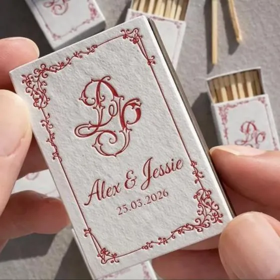 Caja de cerillas de boda con un monograma rojo, nombres y fecha en un marco dibujado