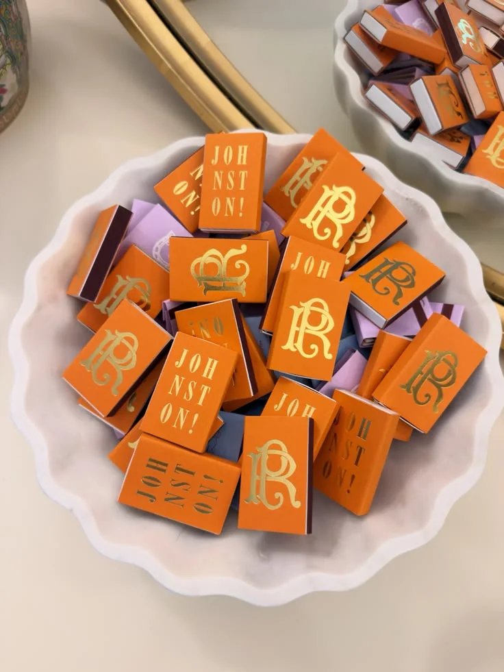 Orange monogram matchboxes piled in a white scalloped bowl