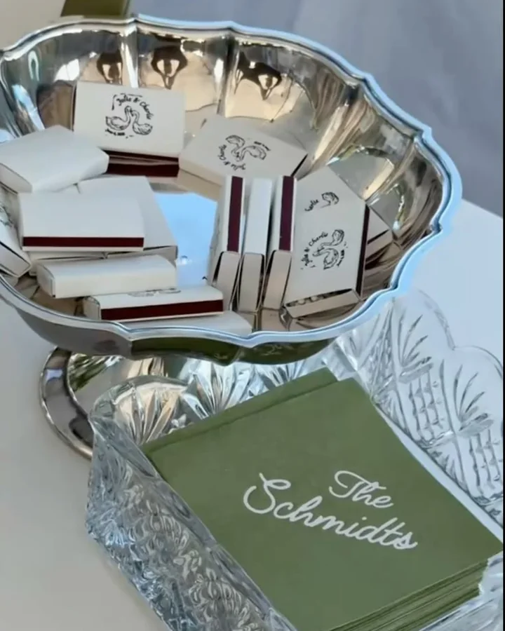 Cajas de cerillas de boda en un cuenco de plata junto a servilletas de cóctel verdes